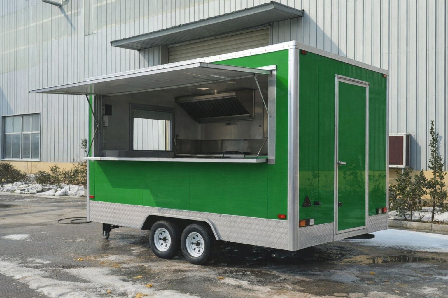 Een moderne groene foodtruck met open verkoopklep op een industrieterrein.