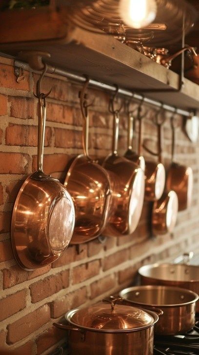 Koperen pannen en kookgerei hangen aan haken tegen een bakstenen muur
