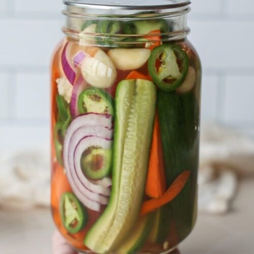 Glazen pot met kleurrijke ingemaakte groenten, waaronder komkommer en wortel