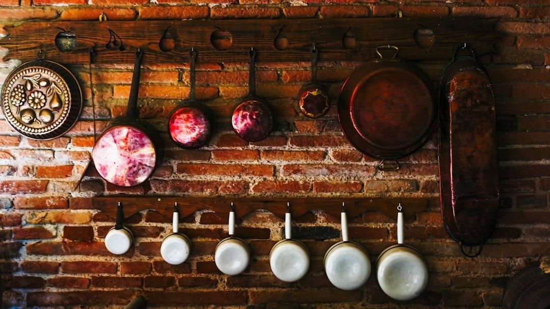 Koperen en gietijzeren pannen hangen aan een houten rek tegen een bakstenen muur